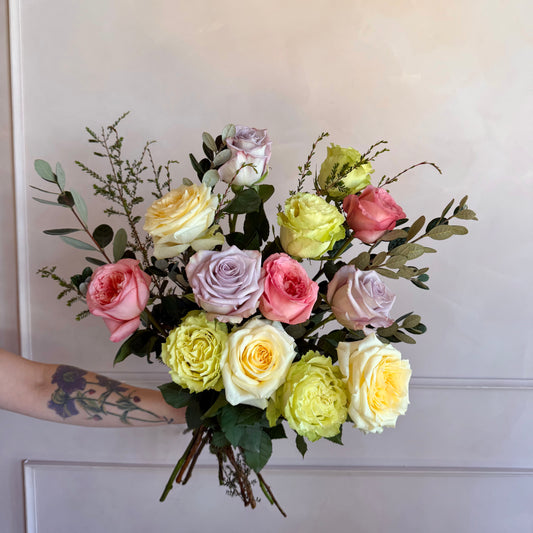 Bouquet of colorful roses held by a person with a tattoo against a white background