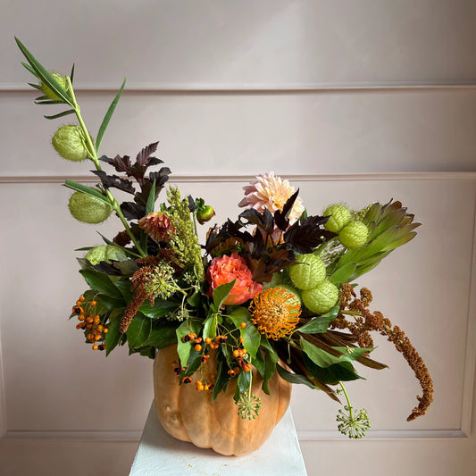 Floral arrangement in a pumpkin container against a neutral background.